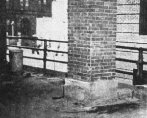 Brick column and iron fence/railing in alley way with view of Elm Street in the background. Investigators theorized that Philip was walking along this fence when he slipped and fell. Dark shading to the right of the column is where Philip’s body was discovered.